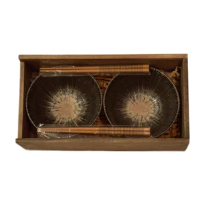 Dos cuencos con dibujo radial sobre fondo oscuro y dos pares de palillos en caja de madera