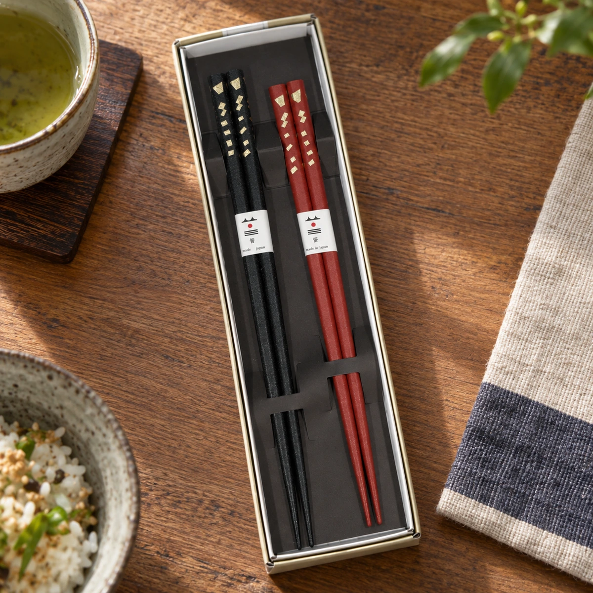 Set de 2 pares de palillos japoneses negros y rojos con motivos dorados en estuche en una escena ilustrativa